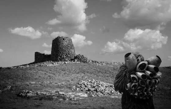 Man with traditional carnival costume of Mamoiada known as "Mamuthones", with his cowbells in front of the Burghidu nuraghe, Ozieri - Sardinia