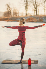 A girl does yoga in winter on the ice of the lake during the sunset