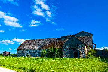 an old stone abandoned building against a blue sky, with a green meadow and a road in the foreground