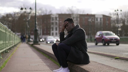 Fototapeta premium Anxious young black man suffering emotional pain sitting on sidewalk in street
