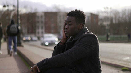 Anxious young black man suffering emotional pain sitting on sidewalk in street