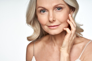 50s mid aged woman touching face skin looking at camera. Attractive mature old woman looking at...
