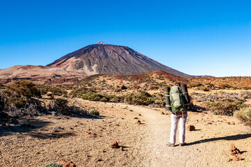 Young woman hiker with backpack looking at Pico del Teide mountain in El Teide National park....