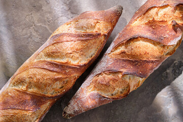 Two freshly baked baguettes on a stone background.