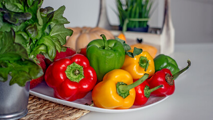 Sweet peppers paprika of red, orange and green color, fruits, lettuce on a plate on the kitchen table, close-up, copy space. Healthy vegan food concept with vitamins and lutein