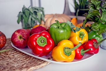 Sweet peppers paprika of red, orange and green color, fruits, lettuce on a plate on the kitchen table, close-up, copy space. Healthy vegan food concept with vitamins and lutein