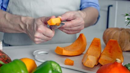 Male hands are cutting an orange pumpkin with a knife on the board at the kitchen table. Home cooking vegan healthy food concept