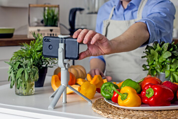 A man without a face, a food blogger, uses his phone to photograph the process of preparing food in his kitchen from vegetables.Concept of making vegan food from natural products at home, self-care, 