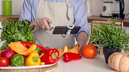 A man without a face, a food blogger, uses his phone to photograph the process of preparing food in his kitchen from vegetables.Concept of making vegan food from natural products at home, self-care, 