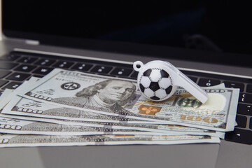 Soccer whistle and dollar banknotes on laptop. Betting on sport concept.