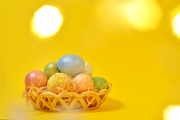 Colorful Easter eggs on a yellow background in a wicker basket in the style of minimalism. with place for text. Easter background with lights. High quality photo