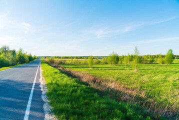 Spring landscape with rural asphalt road with greenery on the sides - 414218730