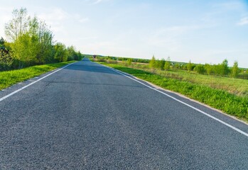 Spring landscape with rural asphalt road with greenery on the sides - 414218769