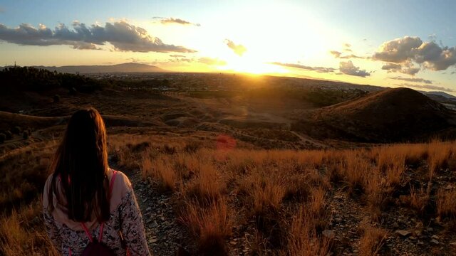 Woman hiking at mountain top against the cityscape of Murcia at sunset.