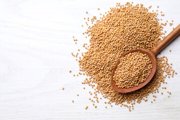 Mustard seeds with wooden spoon on white table, top view. Space for text