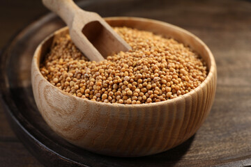 Mustard seeds with wooden bowl and scoop on tray, closeup