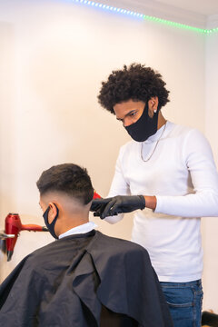 Hairdresser with mask and gloves cutting hair. Security measures of Hairdressers in the Covid-19 pandemic, vertical photo