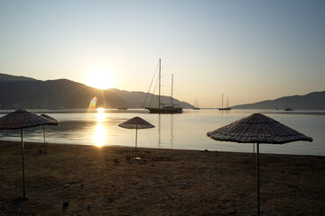 The harbor in the morning with mountains in the background. View to sea with sailing sailboat from sandy beach at dawn.