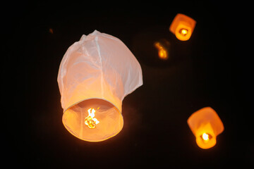 White paper lanterns of desires with a burning candle inside flying up into the night sky.