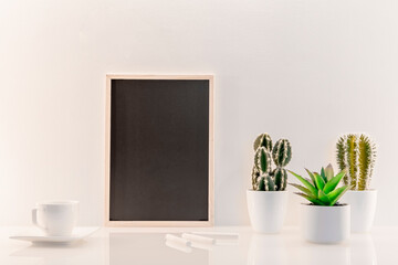 Modèle de tableau noir en ardoise avec espace vide pour logos, inscription publicitaire. Cadre en mode portrait sur un espace de travail avec une tasse à café et des plantes vertes.