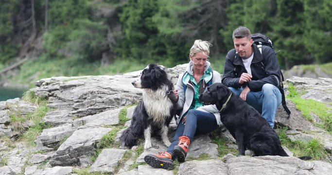 Mature adult couple sitting on rock enjoying nature with dog after walk in forrest, outdoors with scenic views