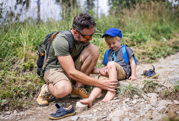 Father with small son on trek outdoors in summer nature, falling and scratched knee concept.