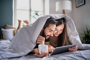 Young couple in love using tablet on bed indoors at home.