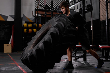 Obraz premium Side view on active man work hard - flipping tire in crossfit training, man using sportive equipment. Cross fit and workout. Strong and handsome athlete.