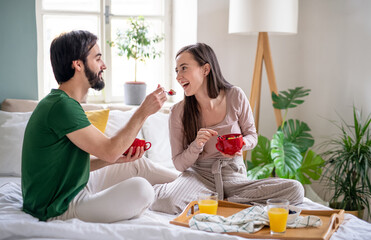 Young couple in love eating breakfast on bed indoors at home.