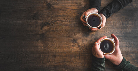 Cups of black tea in the hands of men and women. on a wooden background. with copy space. top view