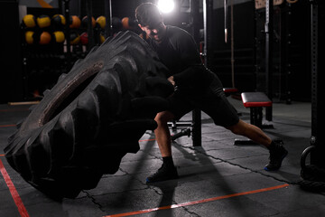 man pushing drawn tire to build strength at modern gym. Male in sportswear is engaged in crossfit...