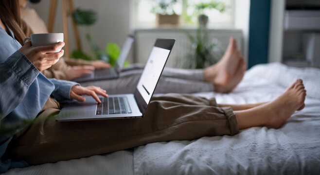 Unrecognizable couple using laptops on bed indoors, home office concept.