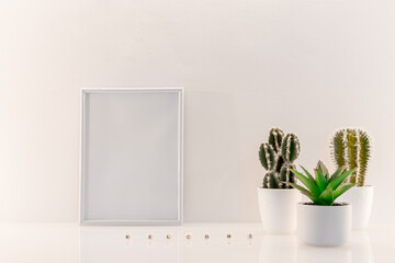 Modèle de cadre photo blanc avec espace vide pour logos, inscription publicitaire. Cadre en mode portrait sur un espace de travail avec des plantes vertes.