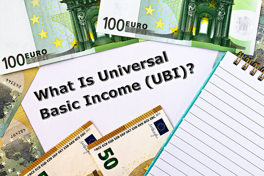 Topview photo on Universal Basic Income theme. The question "What is Universal Basic Income?" on paper, surrounded by euro banknotes and notepad