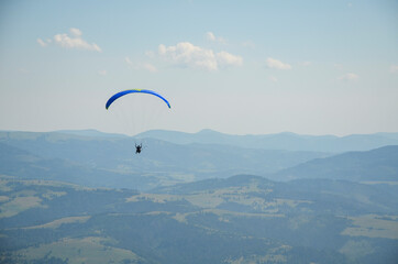 Paraglider flies in the sky over the mountains on a bright sunny day. Paragliding in the sky. Extreme sport.