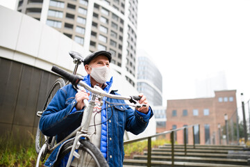 Senior man carrying bicycle outdoors on street in city, coronavirus concept.