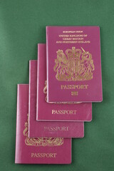Four British passports isolated on a green background, family holiday concept - 414231550