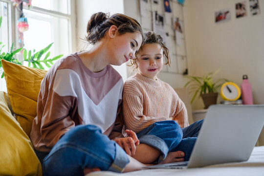 Sisters indoors with laptop at home, watching film. Lockdown concept.