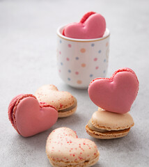 Macarons or French macaroons in heart shapes in a cup on gray background with copy space