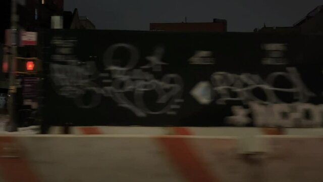 driving past gritty dirty graffiti spray paint tags on boarded up construction site at night New York City NYC