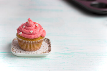muffin with lilac color cream decorated with edible pearls on a saucer stands on a wooden background. Festive cake with cream. cream cheese, butter cream. Fresh bakery. Birthday dessert. small cake. 