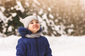 Cute little girl looks at the snow in winter on the street