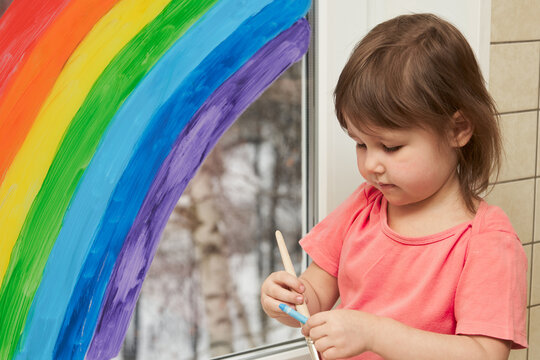 Portrait of a little girl on the background of a rainbow painted on the window.