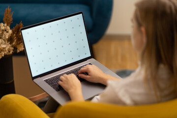 Young student girl writing essay or document on laptop. Living room working, beautiful decors, colorful interior.