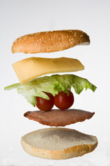 Sandwich made of white buns, meat, tomatoes, cheese, salad arranged horizontally and isolated on a white background. Creative food presentation