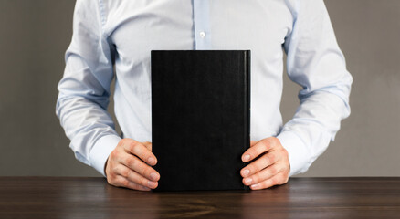 A man in a shirt holds a black book. Businessman