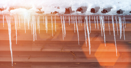 Bright sunbeam falls on icicles hanging on snow covered roof