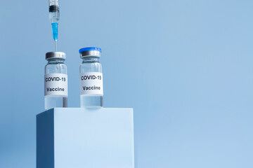 Vial of Covid-19 vaccine  with syringe on  podium . blue  background  . Fashion creative concept .