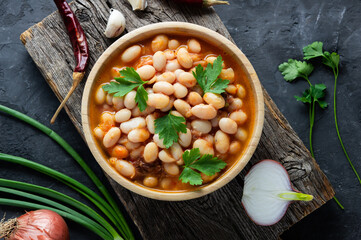 Traditional turkish food,  dried white beans with tomato paste in plate on dark stone background