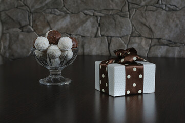 Gift box and round candies in a vase. Composition in brown and white. Selective focus. Daylight